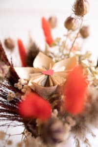 Cette photo représente une composition florale comprenant une fleur de papier en page de roman et des fleurs séchées dans les tons rouges et marrons