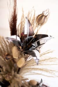 Cette photo représente une composition florale comprenant une fleur de papier et des fleurs séchées dans les tons marrons