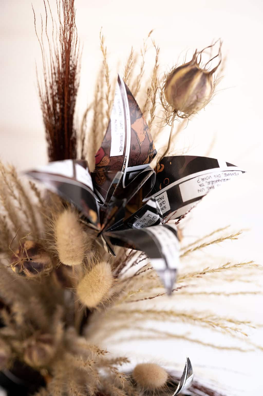 Cette photo représente une composition florale comprenant une fleur de papier et des fleurs séchées dans les tons marrons