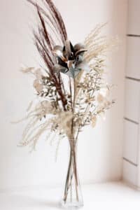 Cette photo représente une grande et haute composition florale comprenant une fleur de papier en forme de double lys et des fleurs séchées dans les tons marrons et beige