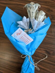 Bouquet de fleurs de papier réalisé à partir de partitions musicales et enveloppé dans une feuille de papier de soie bleu