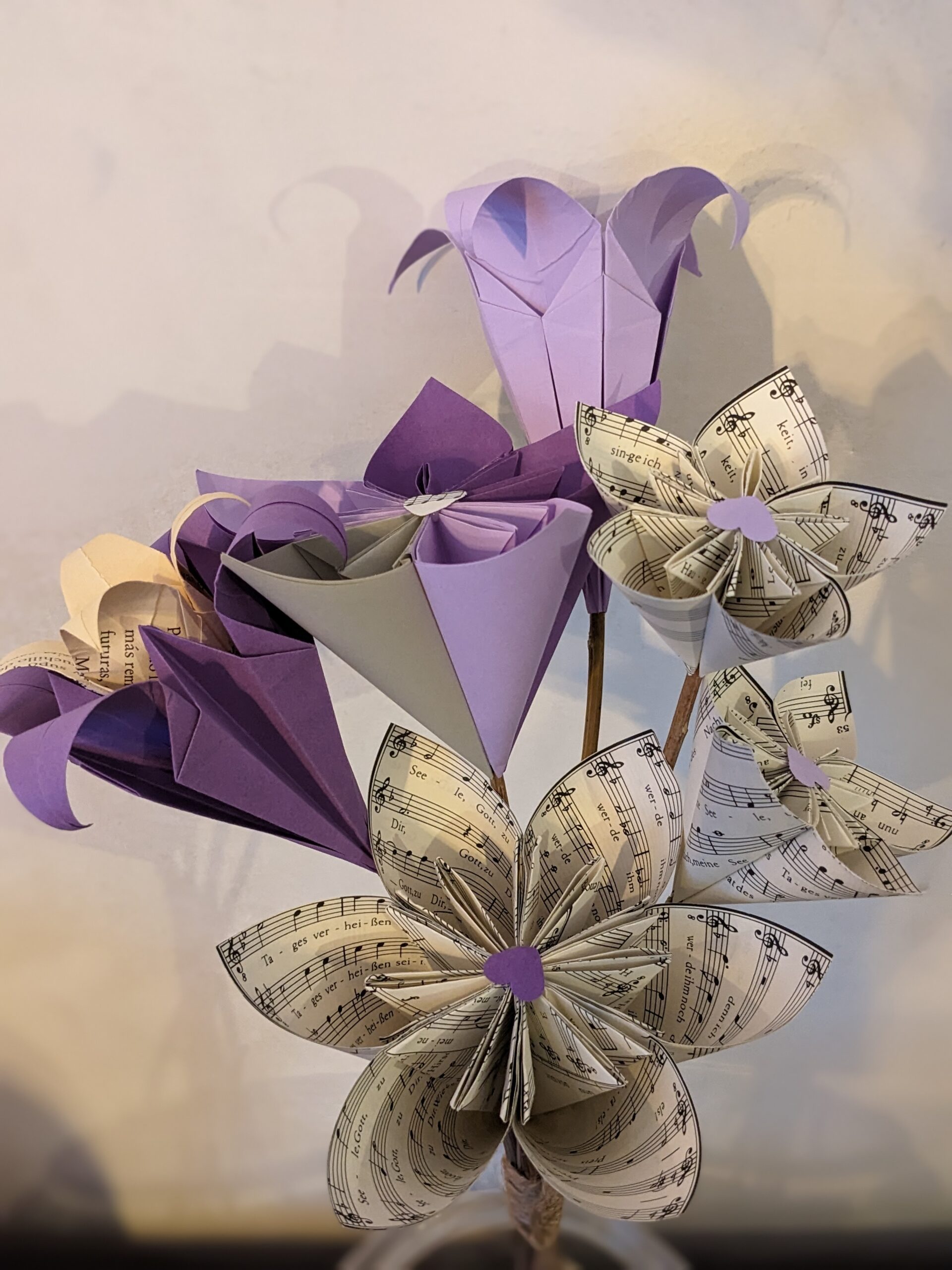 Cette photo représente un gros bouquet de fleurs de papier réalisé à partir de papier de différentes teintes violettes et de partitions musicales.