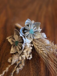 Cette photo représente une barrette à chignon et une boutonnière assorties alliant de la fleur séchées et fleurs de papier dans les tons vert et beige