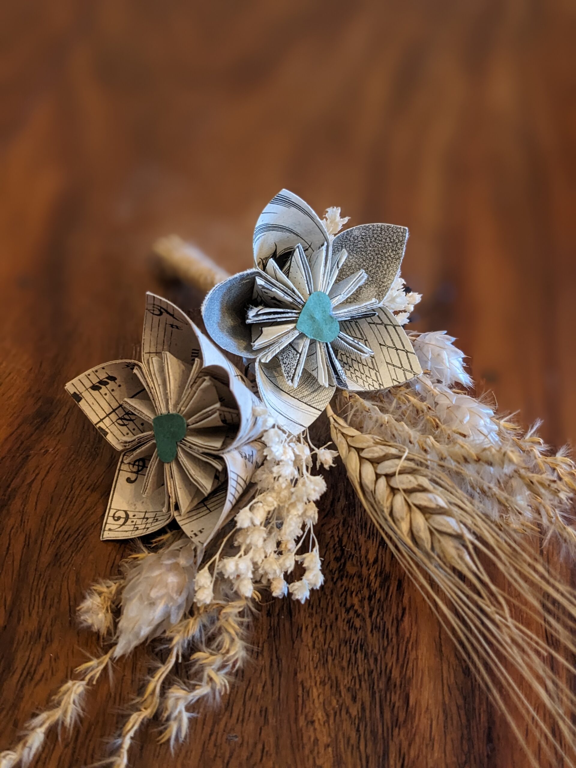 Cette photo représente une barrette à chignon et une boutonnière assorties alliant de la fleur séchées et fleurs de papier dans les tons vert et beige