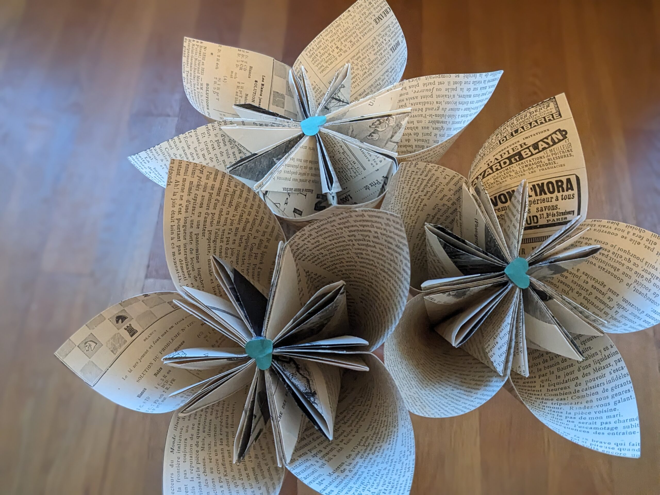 Trois grosses fleurs de papier en pages de romans des années 1890, avec un cœur vert au milieu de chaque fleur