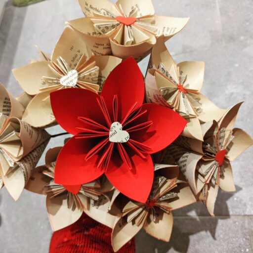 Cette photo représente un bouquet de fleurs de papier réalisé majoritairement avec des vieilles pas de romans et une grosse fleur en papier rouge vif au milieu